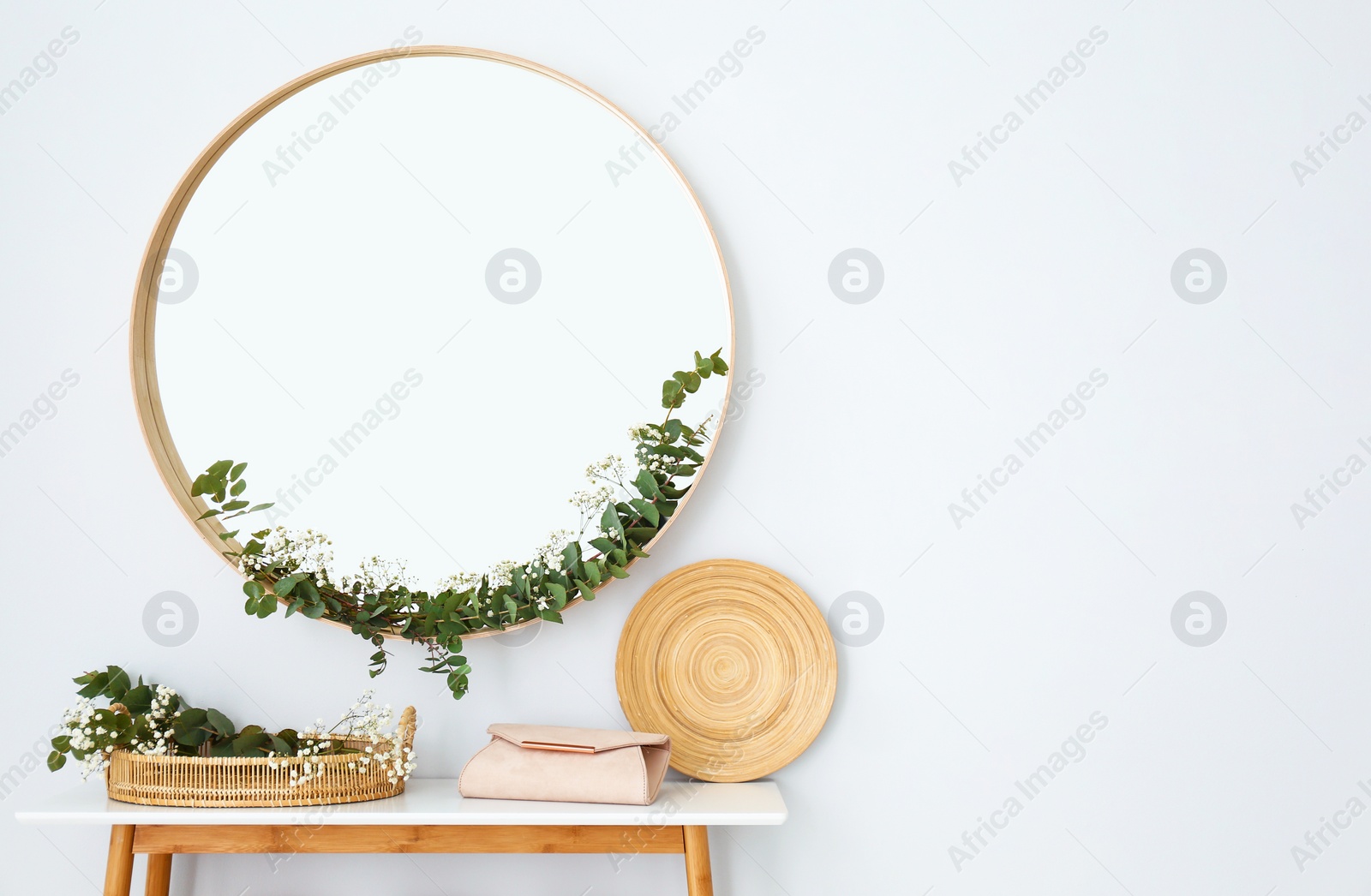 Photo of Round mirror and table with accessories near white wall. Modern interior design