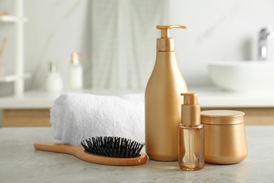 Different hair care products, towel and brush on table in bathroom