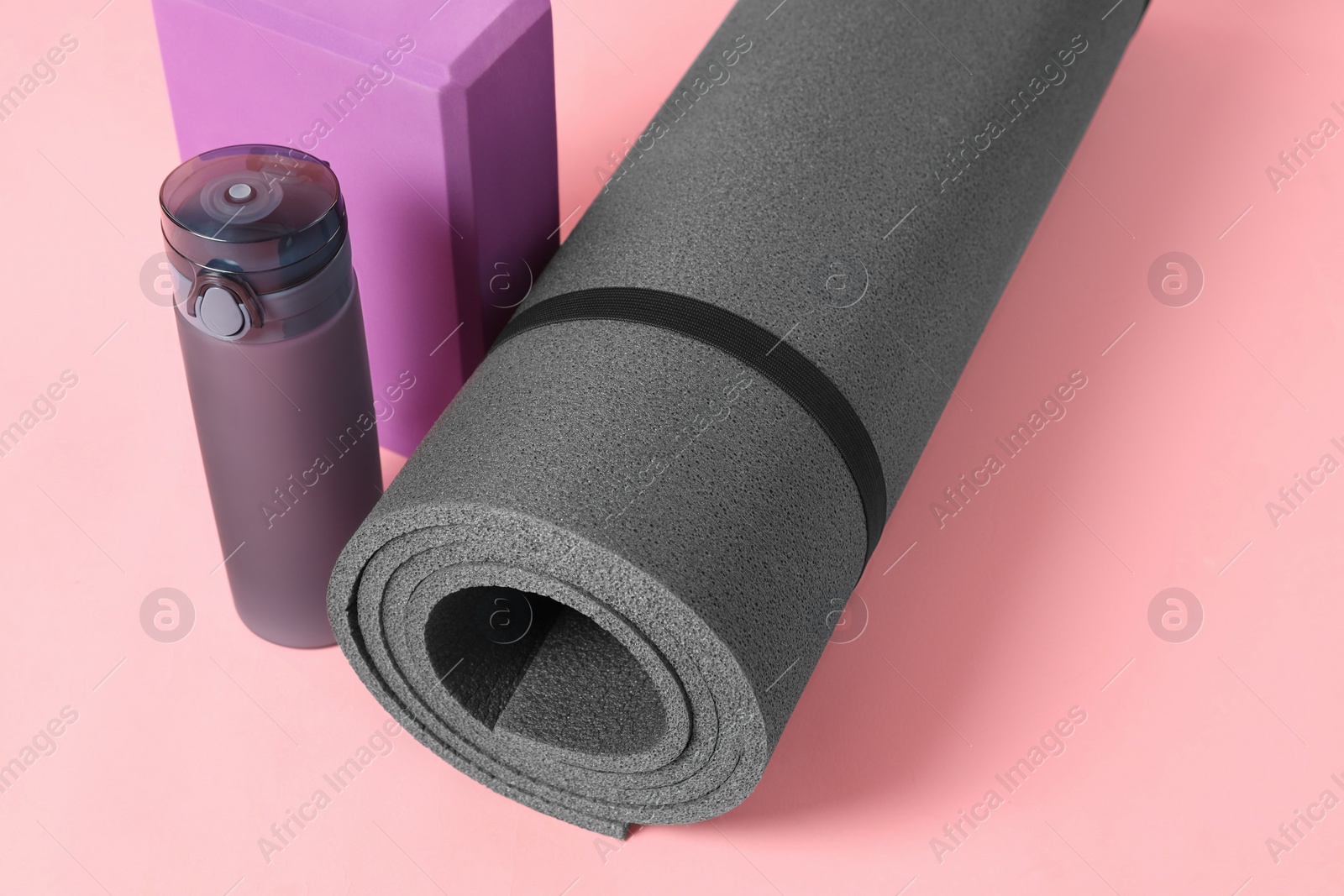 Photo of Grey exercise mat, yoga block and bottle of water on pink background