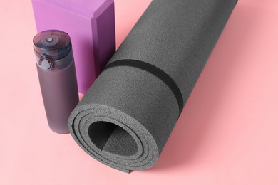 Photo of Grey exercise mat, yoga block and bottle of water on pink background