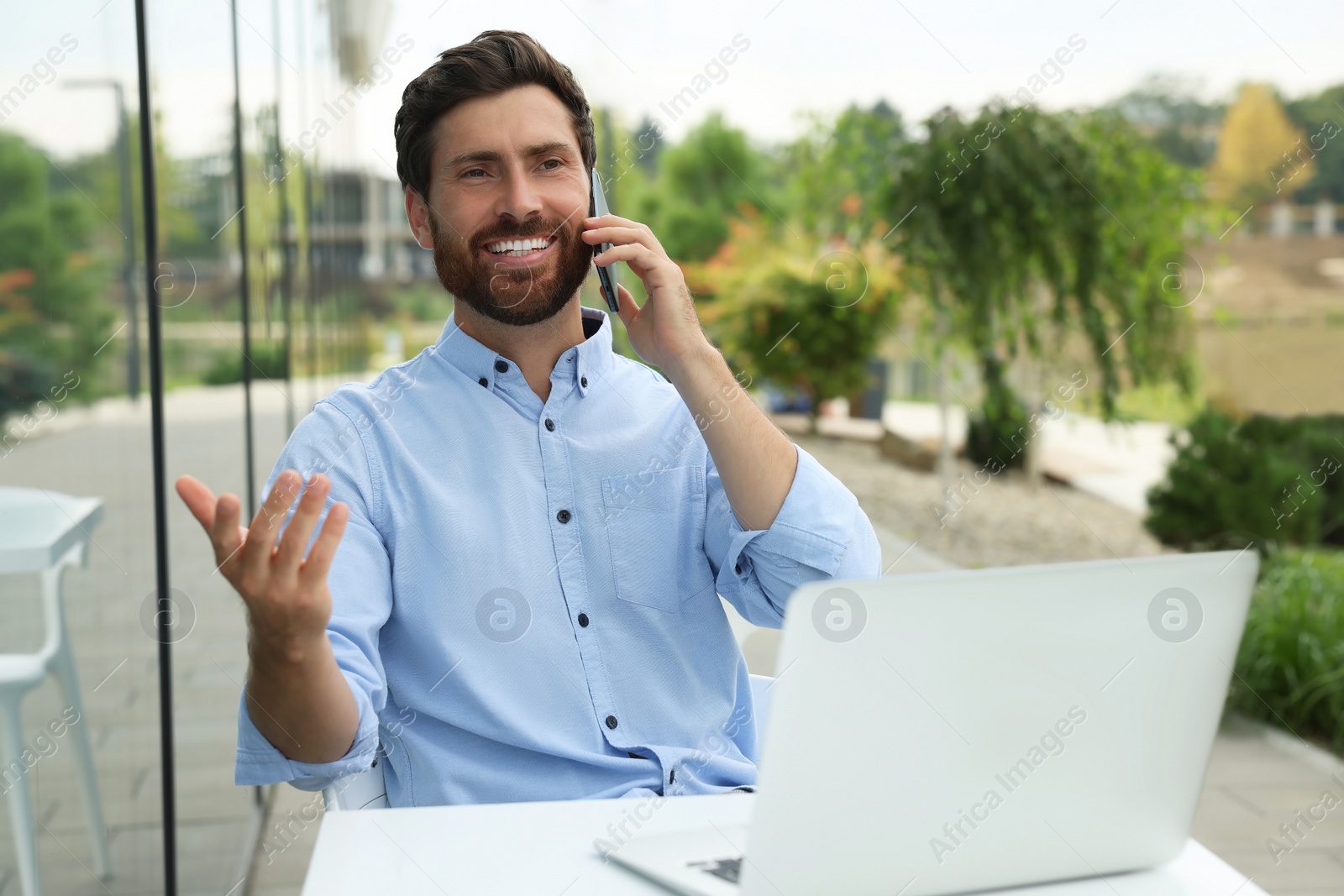 Photo of Handsome man with laptop talking on phone in outdoor cafe