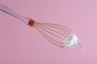Photo of Whisk with whipped cream on pink background