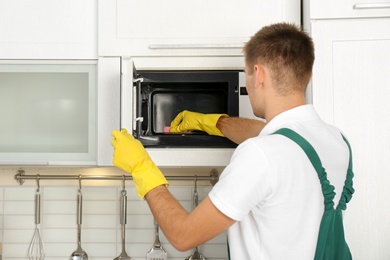Photo of Male janitor cleaning microwave oven in kitchen