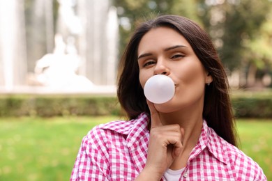 Photo of Beautiful young woman blowing chewing gum outdoors, space for text