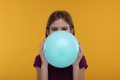 Photo of Girl inflating bright balloon on orange background