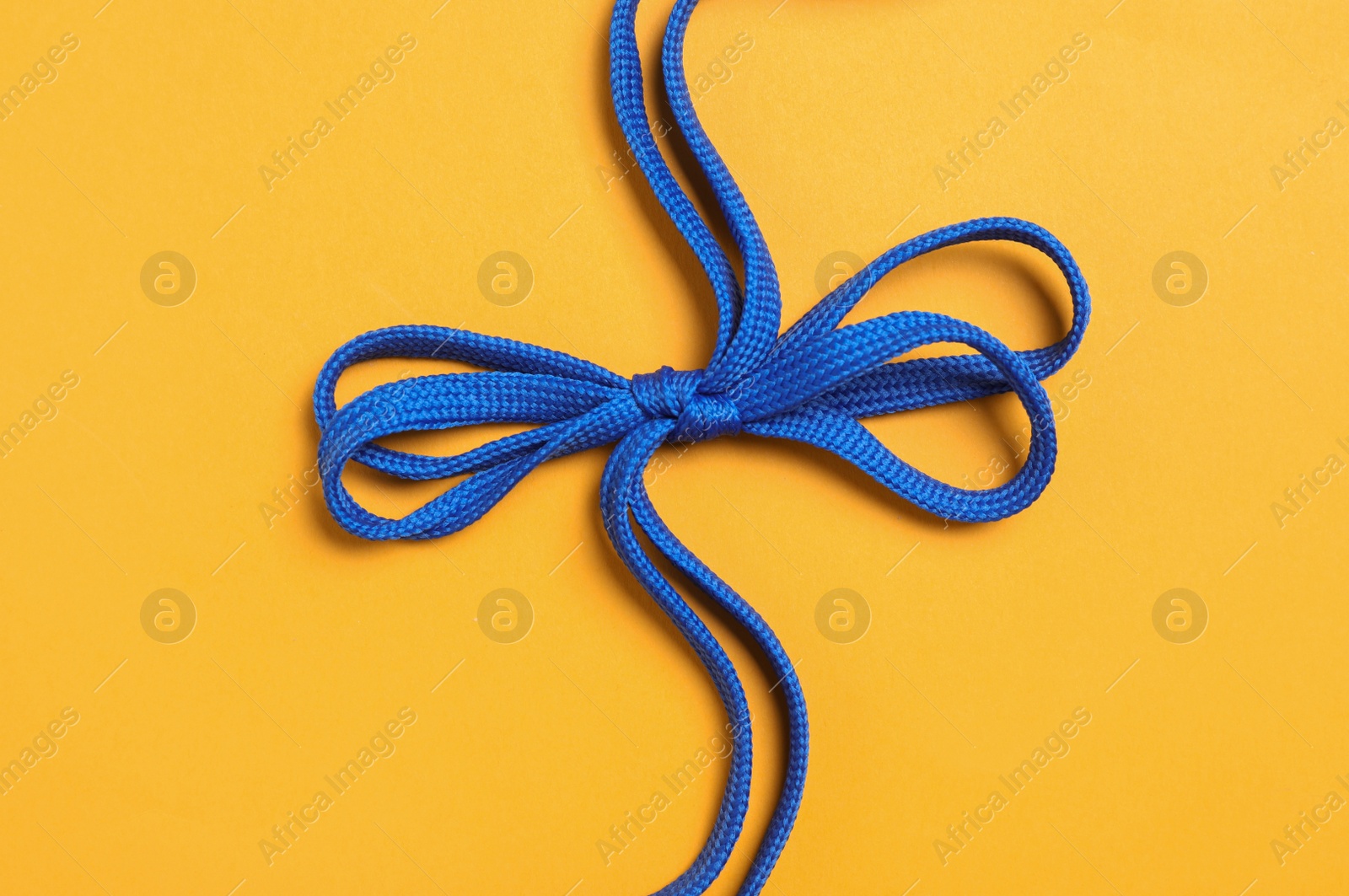 Photo of Blue shoelaces on yellow background, top view