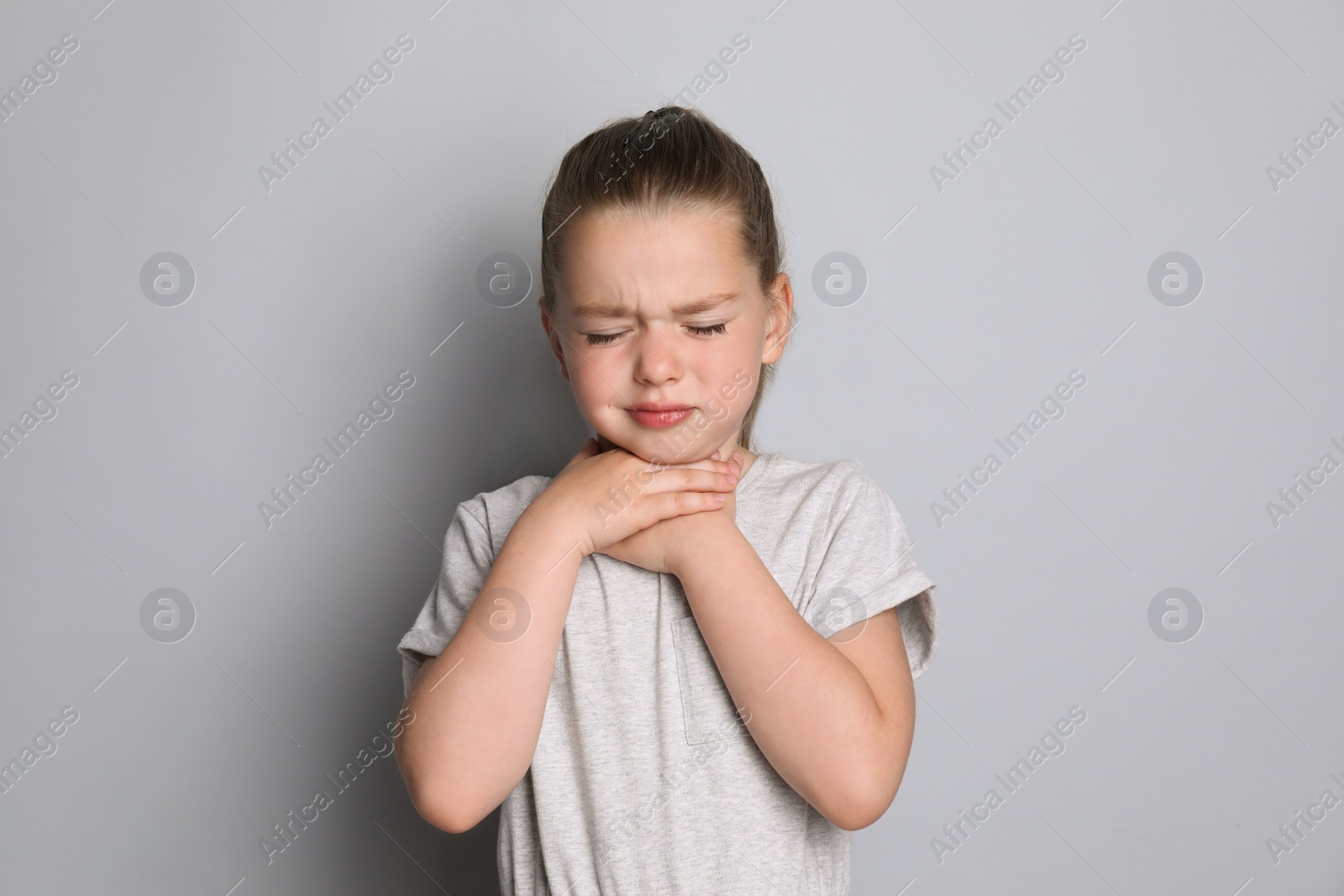 Photo of Little girl suffering from sore throat on grey background