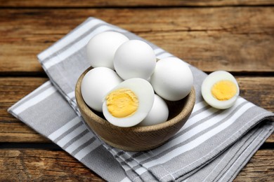 Photo of Bowl with hard boiled eggs and kitchen towel on wooden table