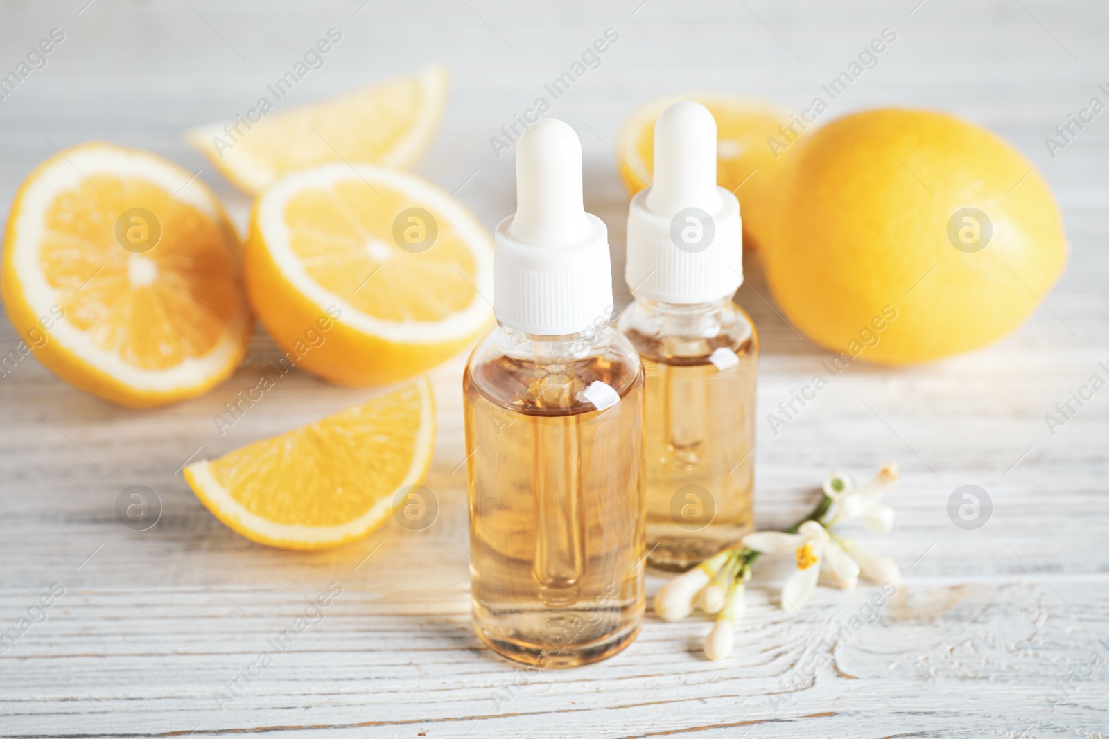 Photo of Bottles of citrus essential oil, flower and lemons on white wooden table