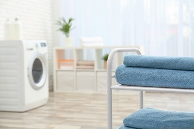 Folded clean terry towels on shelving unit in laundry room, space for text