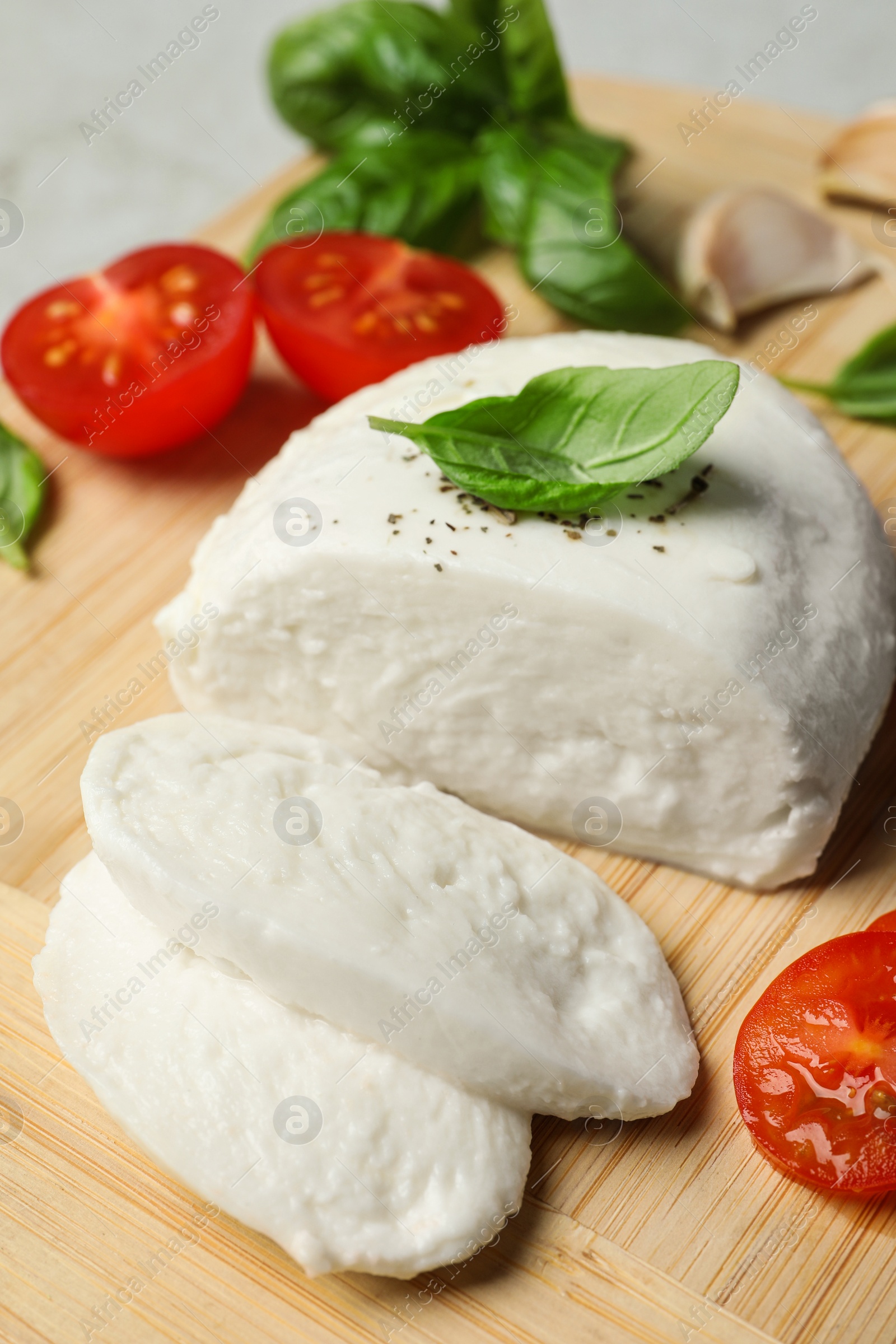 Photo of Delicious mozzarella with tomatoes and basil leaves on wooden board, closeup