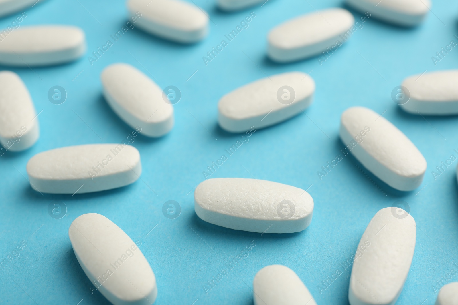 Photo of Vitamin pills on light blue background, closeup