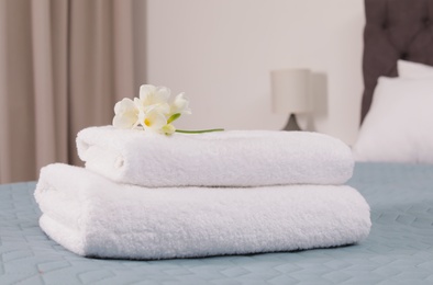 Photo of Stack of fresh towels with flowers on bed in hotel room