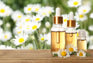 Image of Bottles of essential oil and chamomile flowers on wooden table against blurred background. Space for text