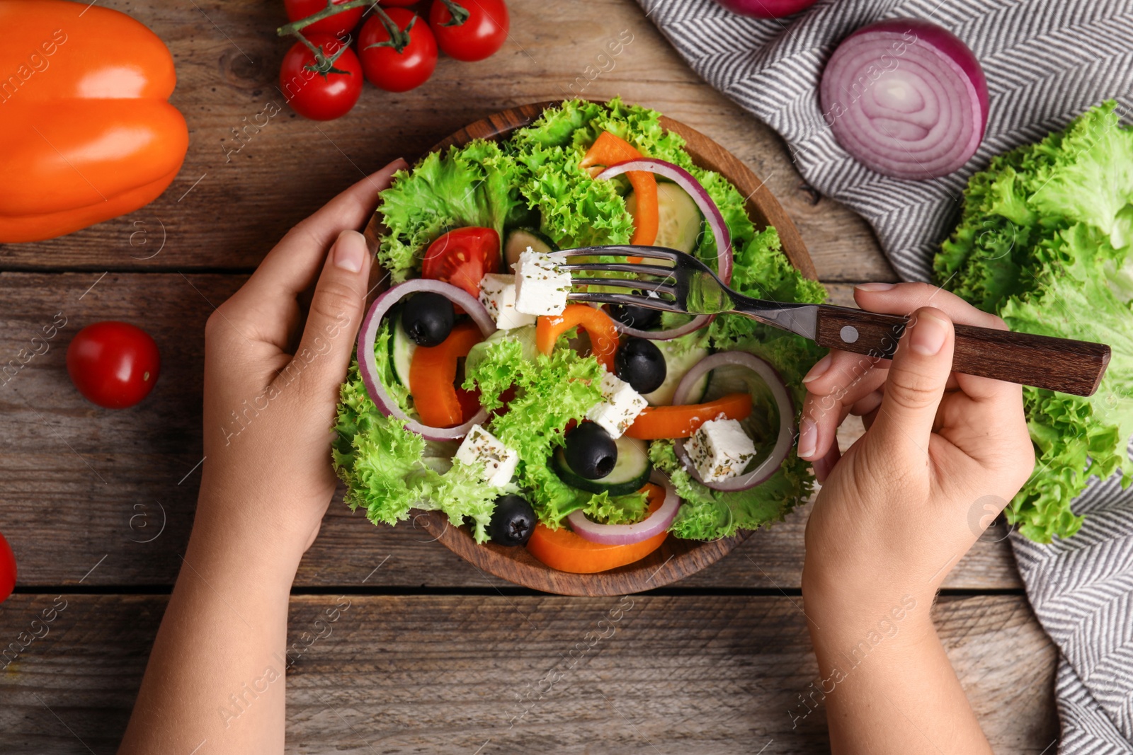 Photo of Woman eating tasty fresh Greek salad at wooden table, top view