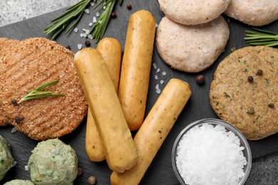 Photo of Different raw vegan meat products, salt and rosemary on dark board, flat lay