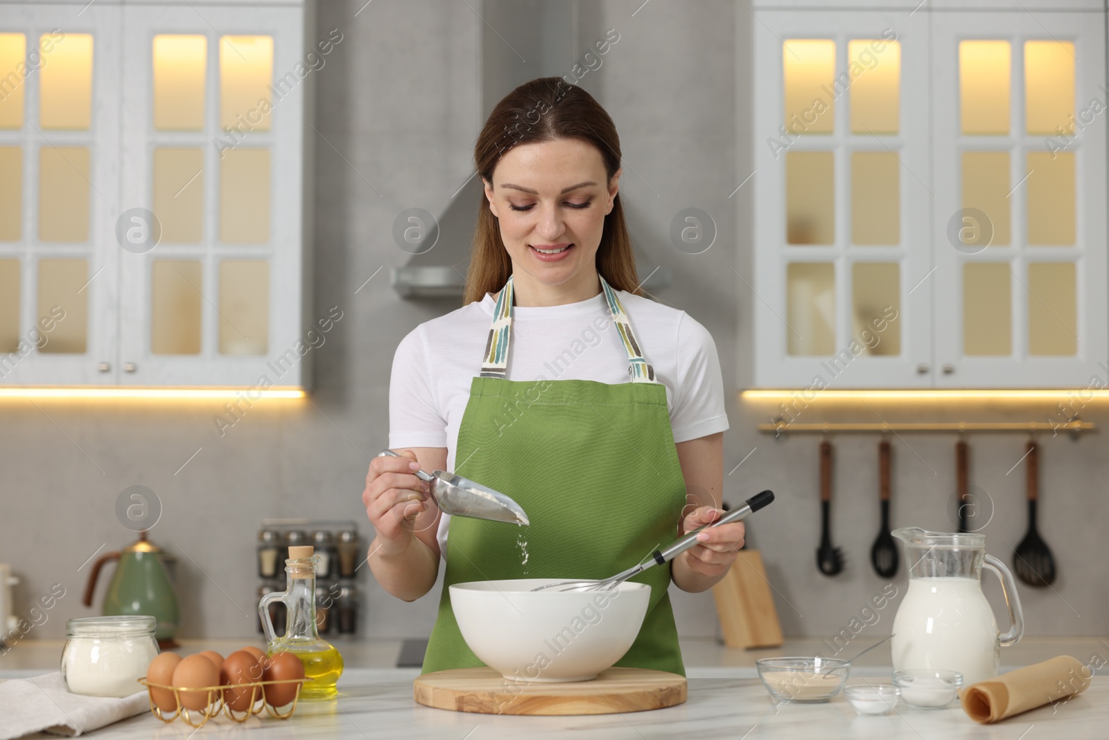 Photo of Making bread. Woman putting flour into bowl at white table in kitchen