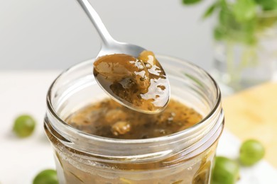 Photo of Spoon over jar with delicious gooseberry jam, closeup
