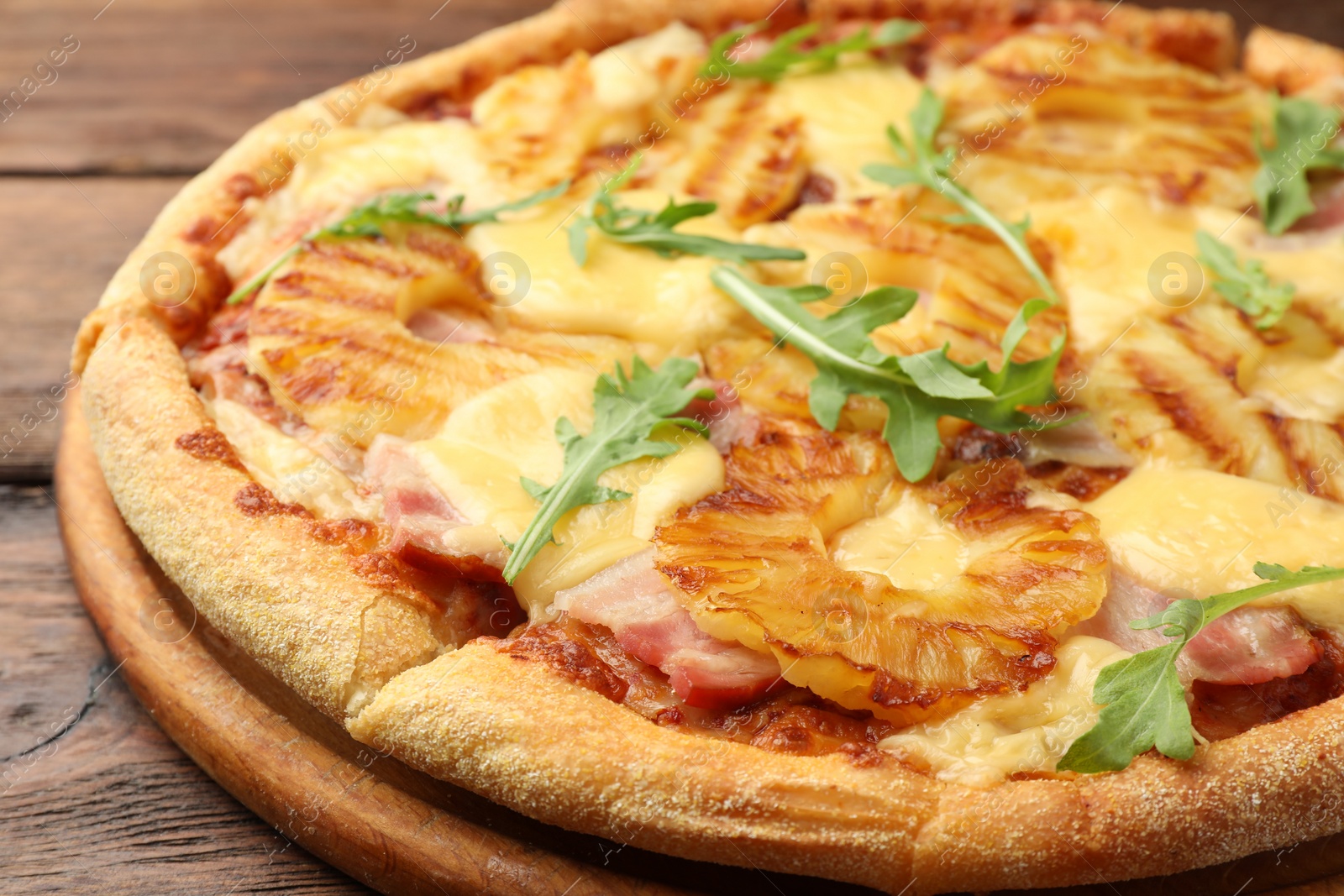 Photo of Delicious pineapple pizza with arugula on wooden table, closeup