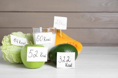 Photo of Food products with calorific value tags on white wooden table, space for text. Weight loss concept