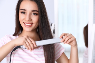 Happy woman using hair iron at home