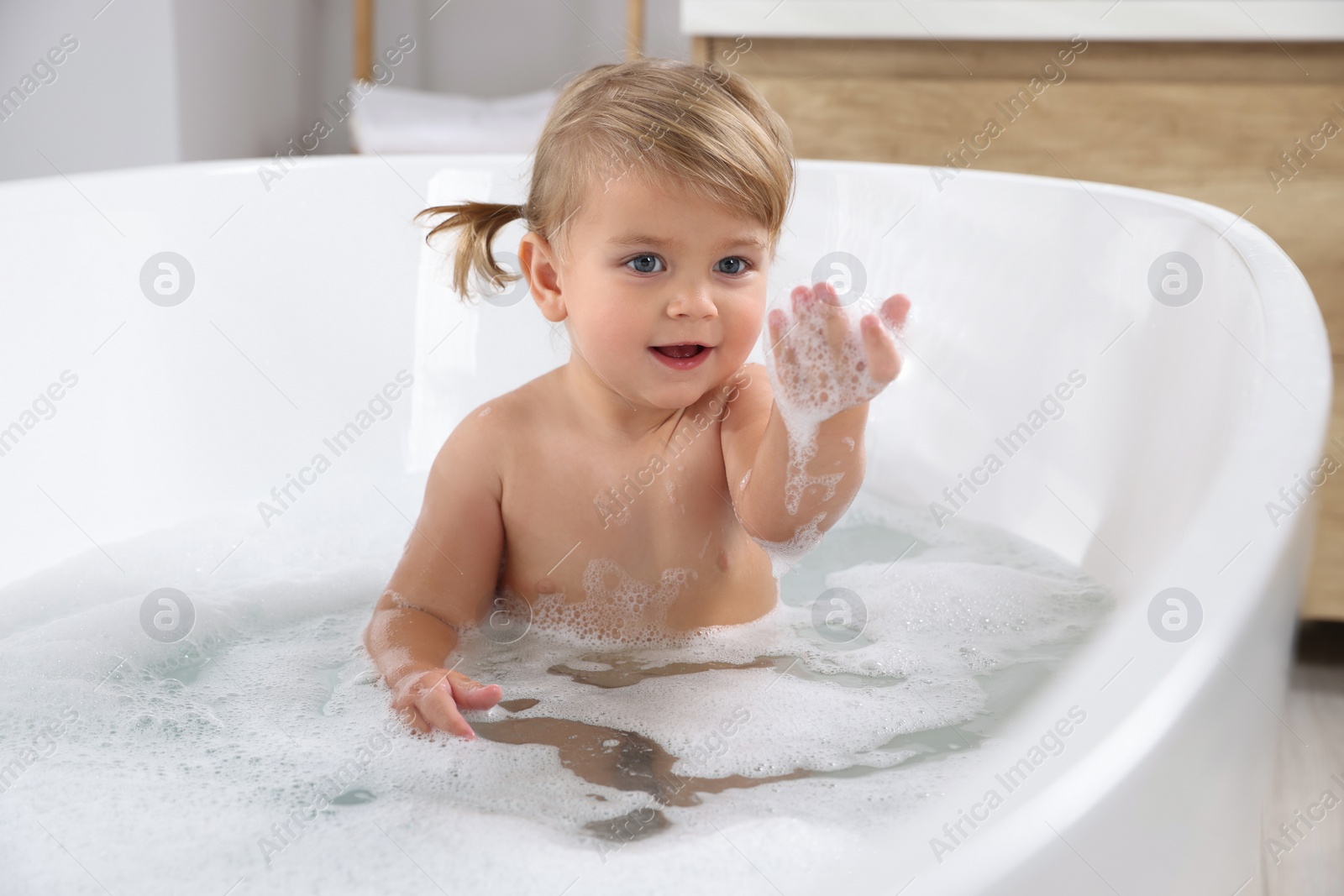 Photo of Cute little girl taking foamy bath at home