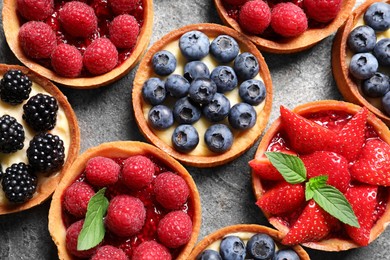 Photo of Tartlets with different fresh berries on light grey table, flat lay. Delicious dessert