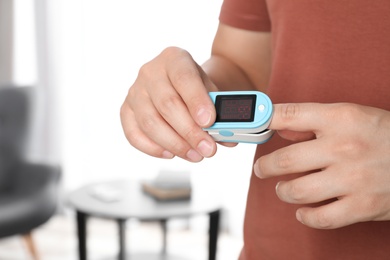 Photo of Young man checking pulse with blood pressure monitor on finger indoors, closeup