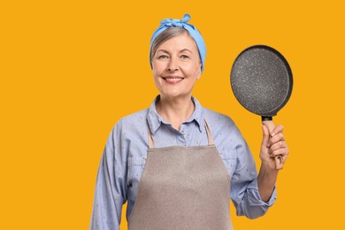 Photo of Happy housewife with frying pan on orange background
