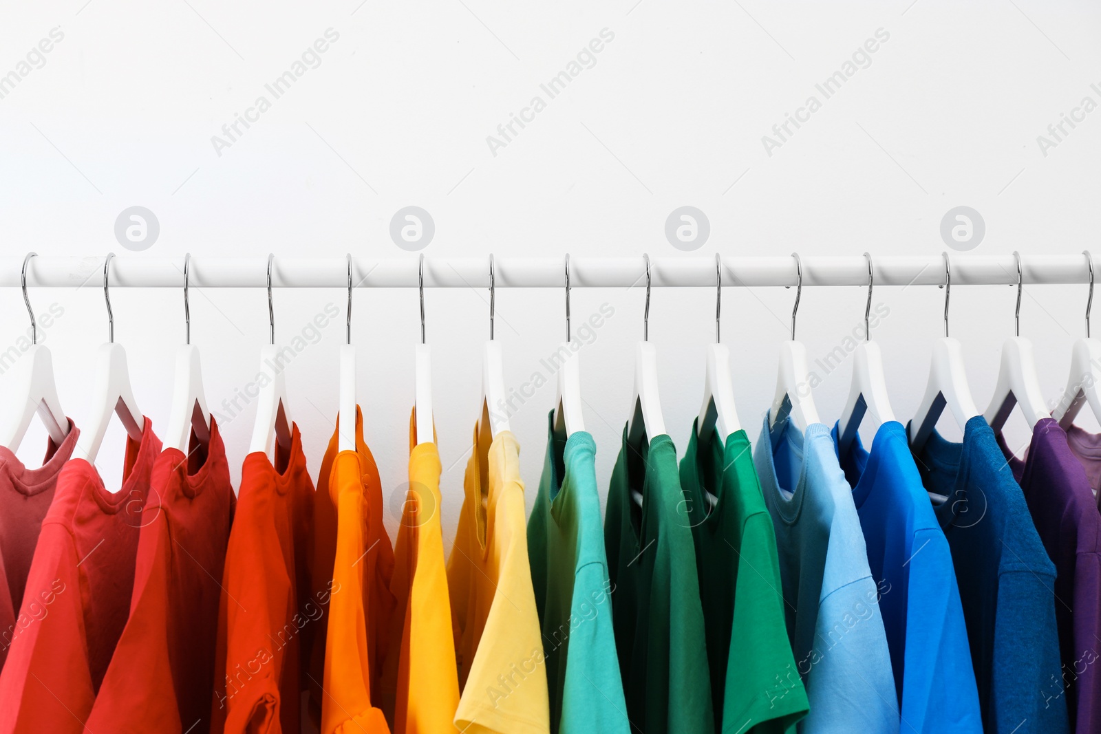 Photo of Rack with bright clothes on white background. Rainbow colors