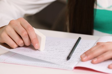 Photo of Girl erasing mistake in her notebook at white desk, closeup