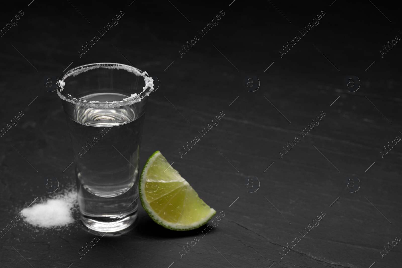 Photo of Mexican Tequila shot with salt and lime slice on black table. Space for text