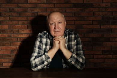 Poor senior man sitting at table near brick wall