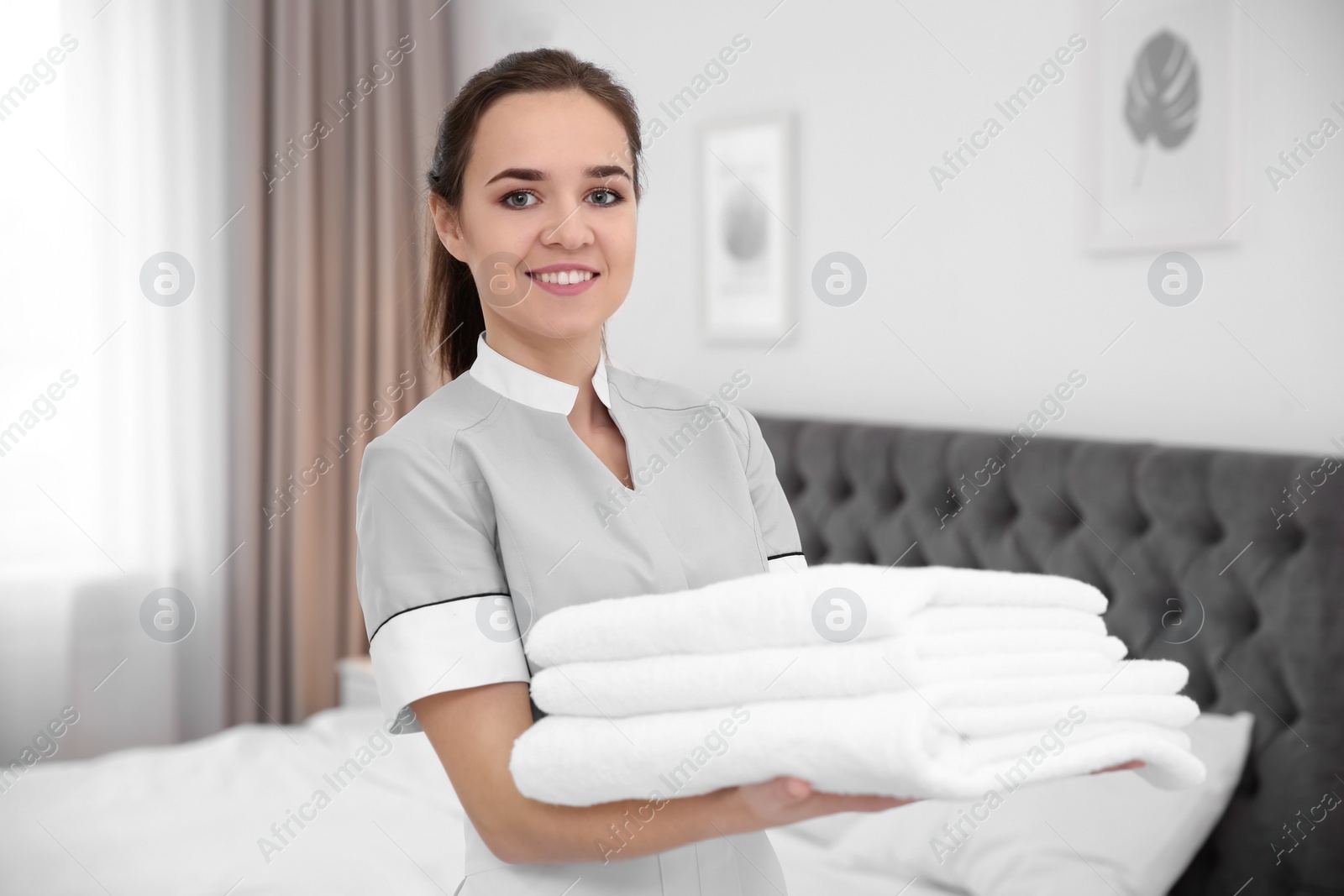 Photo of Young maid holding stack of towels in hotel room