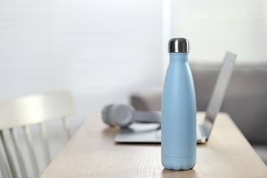 Stylish thermo bottle and laptop on wooden table at home. Space for text
