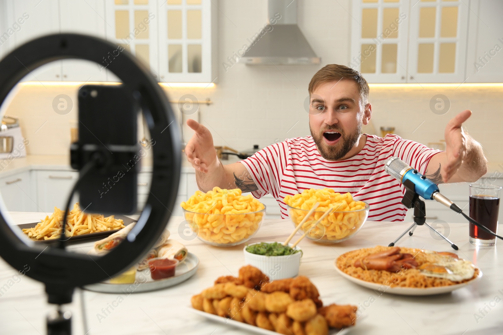 Photo of Emotional food blogger recording eating show on smartphone camera in kitchen. Mukbang vlog