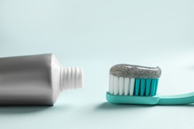 Photo of Brush with charcoal toothpaste and tube on light background, closeup