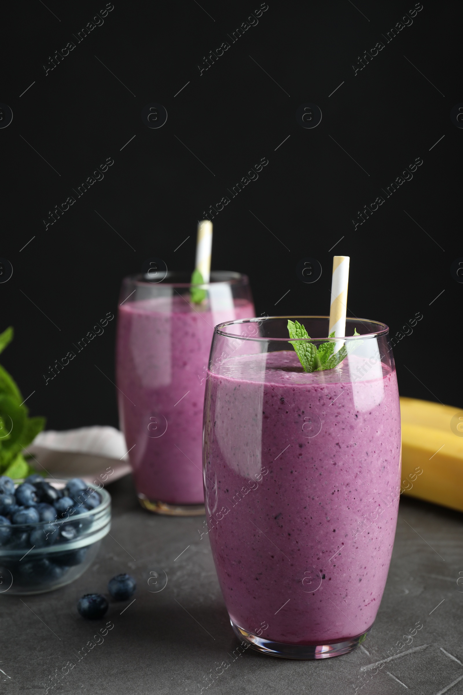 Photo of Glasses of delicious blueberry smoothie on grey table against black background