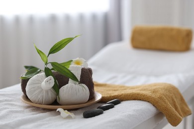 Photo of Spa stones, flowers, towel and herbal bags on massage table indoors