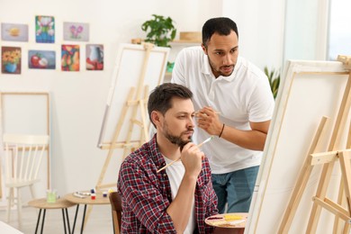 Photo of Artist teaching his student to paint in studio. Creative hobby