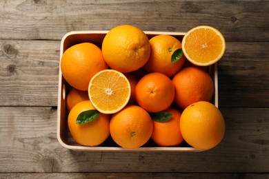 Photo of Many whole and cut ripe oranges on wooden table, top view