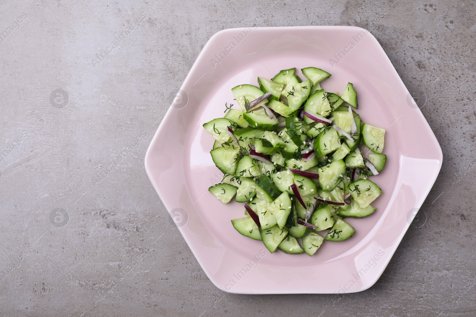 Photo of Plate of vegetarian salad with cucumber and onion on grey background, top view. Space for text