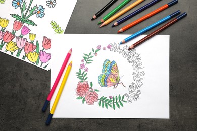Photo of Coloring pages with children drawings and set of pencils on grey table, flat lay