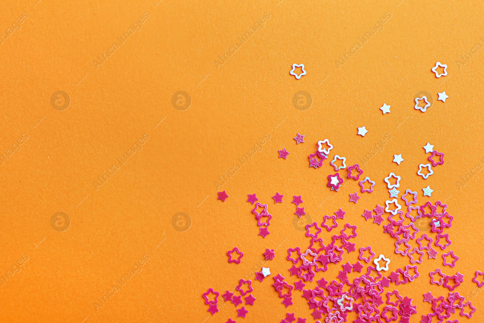 Photo of Shiny bright star shaped glitter on pale orange background. Space for text