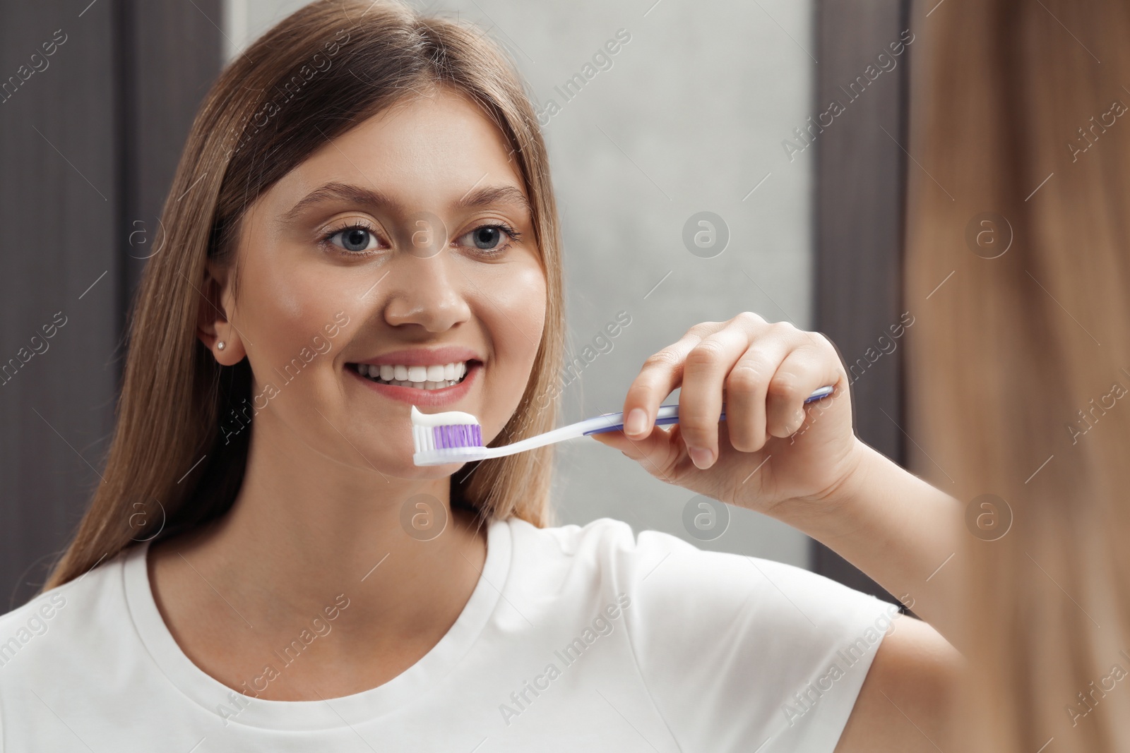 Photo of Young woman holding brush with toothpaste near mirror in bathroom