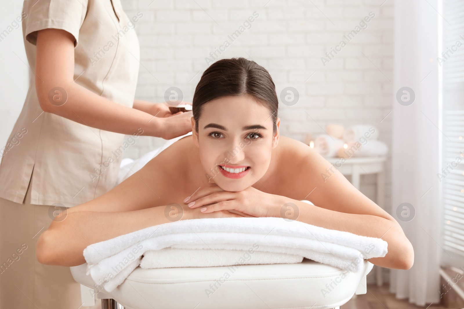 Photo of Young woman having body scrubbing procedure with sea salt in spa salon