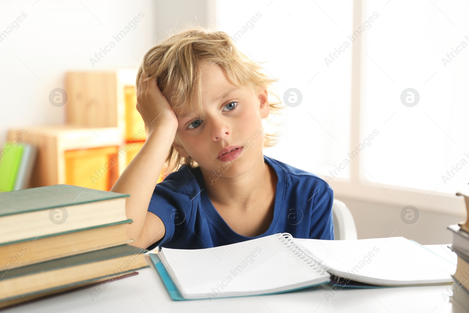 Photo of Sad little boy doing homework at table indoors