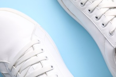 Pair of stylish white sneakers on light blue background, top view