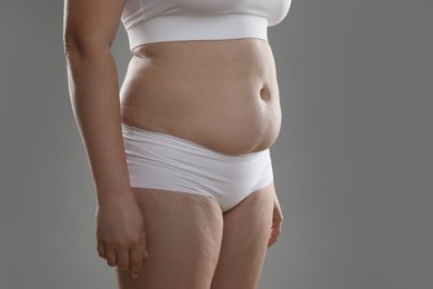 Woman with excessive belly fat on grey background, closeup. Overweight problem