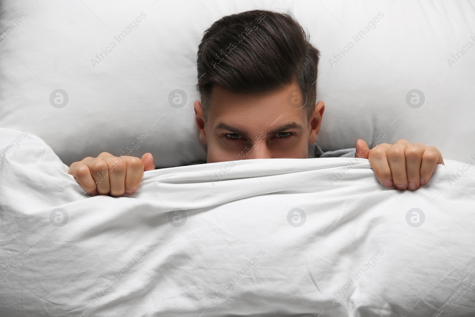 Photo of Handsome man covering his face with blanket while lying in bed at home